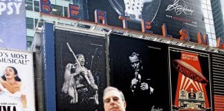 George Kalinsky, formerly of Port Washington and Sands Point, stands before his images of Jimi Hendrix and Frank Sinatra in Times Square in an undated photograph. (Photo courtesy of Lee Kalinsky)